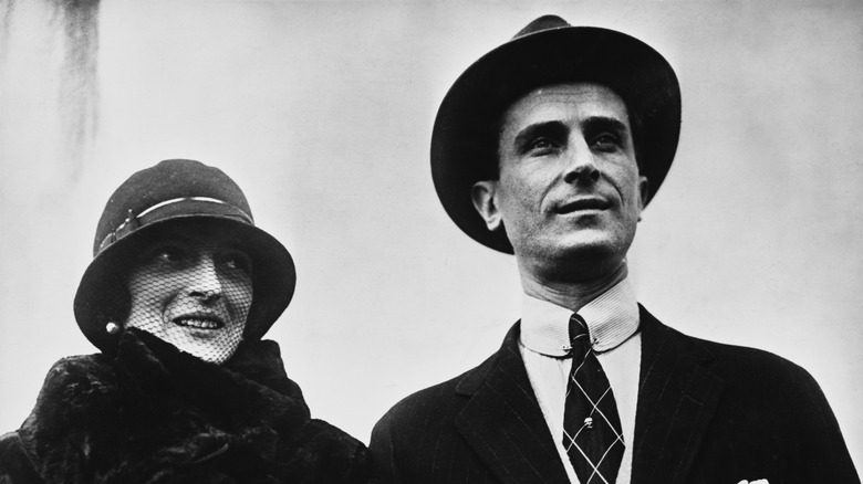 Felix Yusupov and wife smiling wearing black hats and smart dark clothing