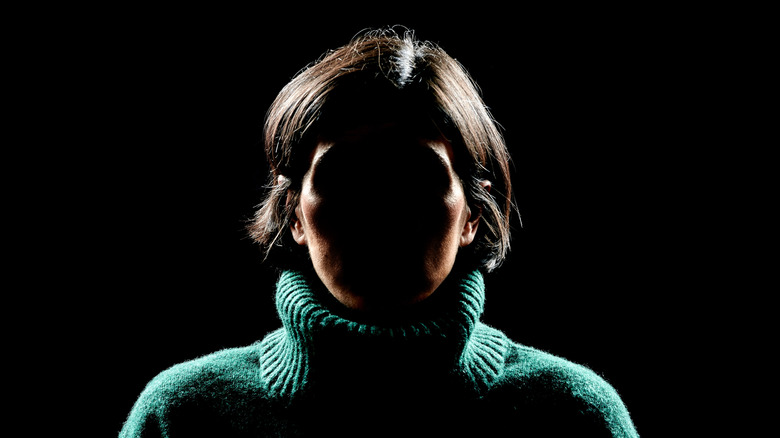 a woman in a green shirt with a shadowed face against a black background