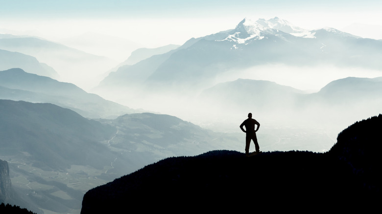 Silhouette of person standing on ridge with snow-capped mountains in distance