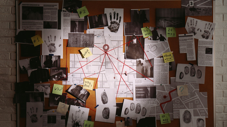 Detective board with fingerprints, photos, map and clues connected by red string on white brick wall
