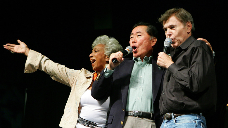 nichelle nichols, walter koenig, and george takei singing onstage