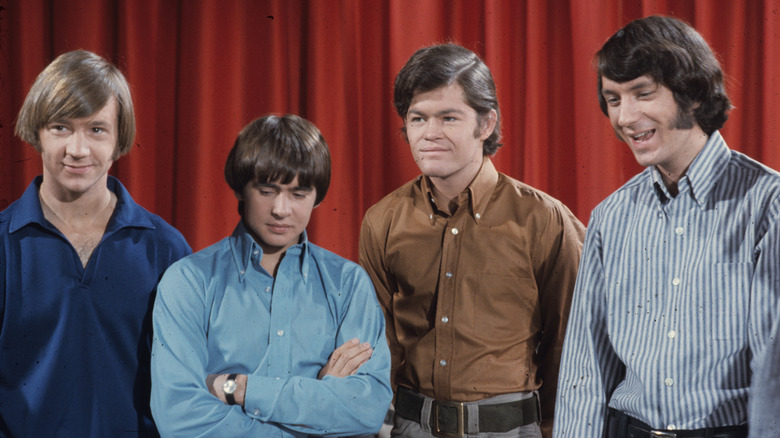 The Monkees stood together in front of a red curtain