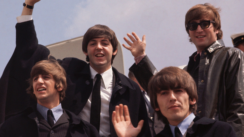The Beatles getting off a plane and waving in the 1960s