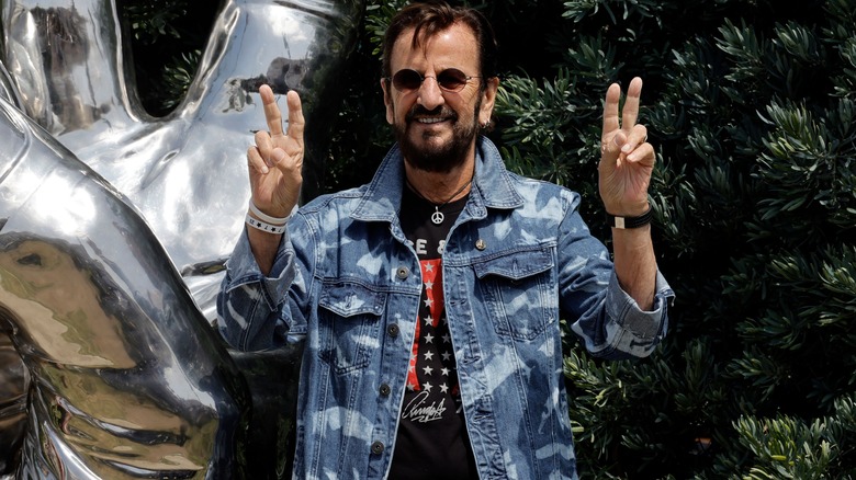 Ringo Starr giving peace signs outside