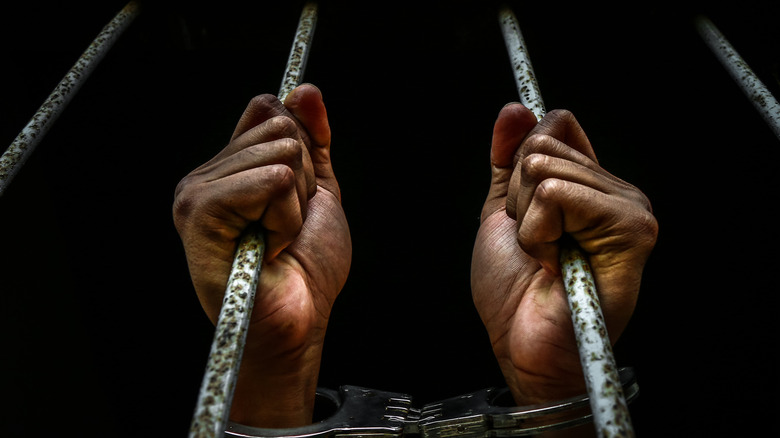 handcuffed hands holding jail bars