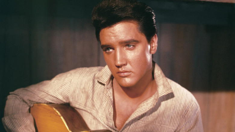 Elvis Presley sitting and holding acoustic guitar on set