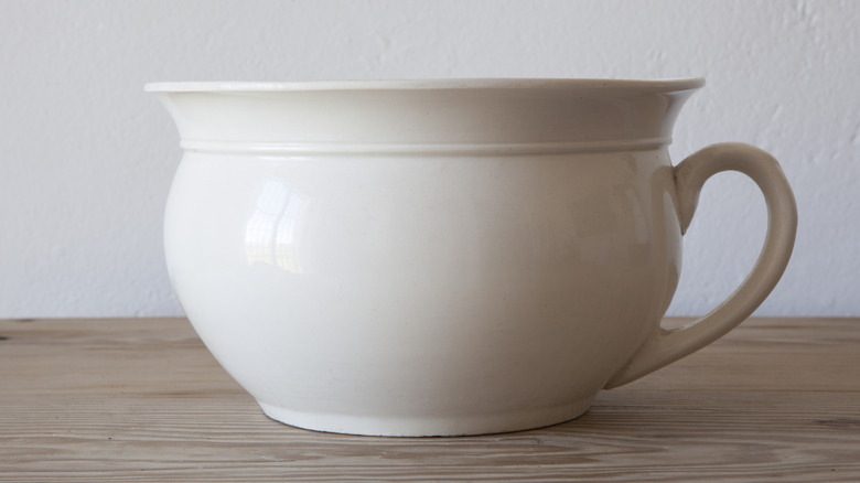 A white porcelain chamber pot on a wooden surface
