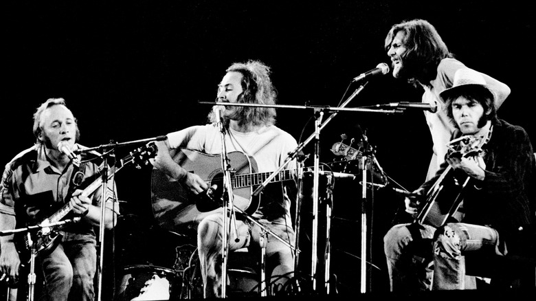 Crosby, Stills, Nash and Young singing into microphones on stage in the 70s