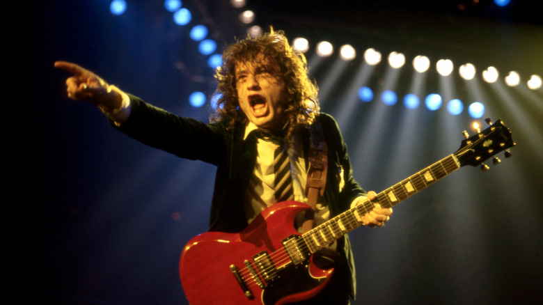 Angus Young of AC/DC playing guitar on stage in the '80s with Brian Johnson in background
