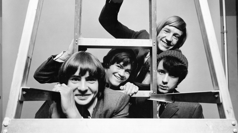 Black and white photo of the Monkees staring through a ladder on the set of their television show in 1967