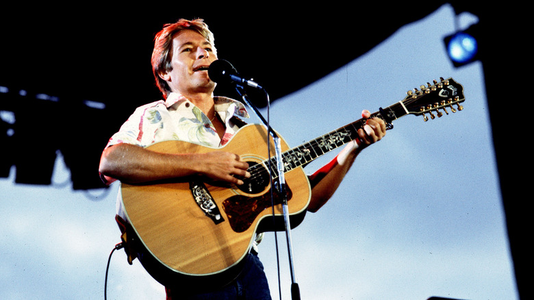 John Denver playing acoustic guitar and singing on stage