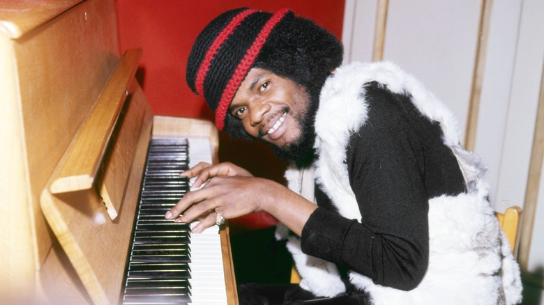 Billy Preston smiling and playing piano in woolen hat
