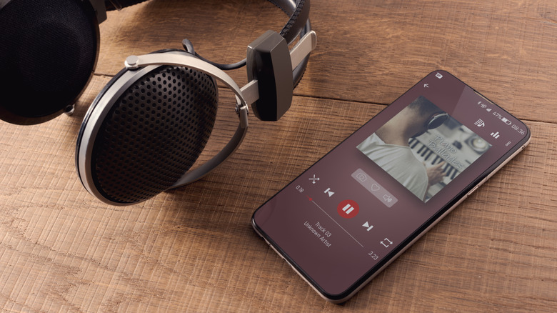 a smartphone lying beside headphones on wooden surface