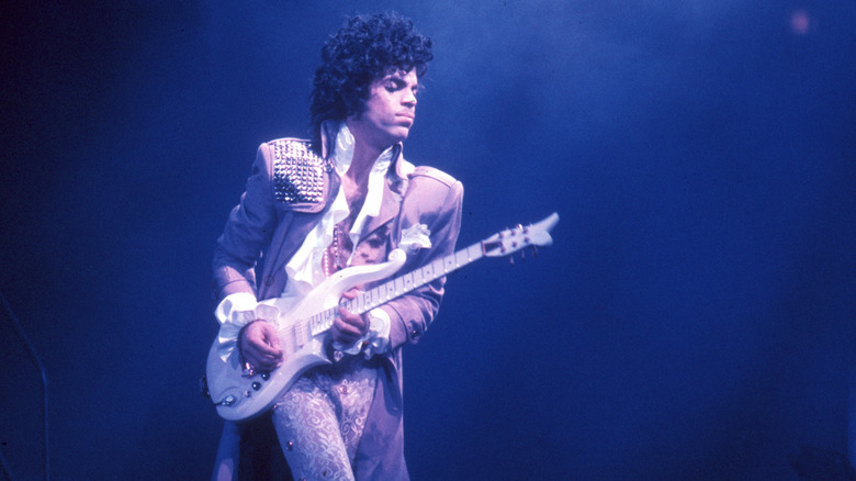 Prince playing guitar in concert against blue background
