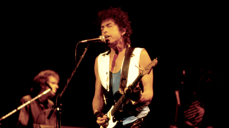 Bob Dylan playing electric guitar and singing into microphone onstage