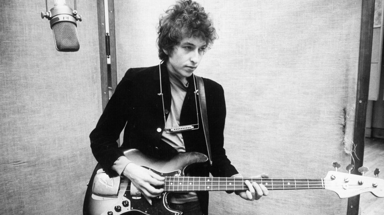 Bob Dylan with guitar and harmonica in recording studio booth