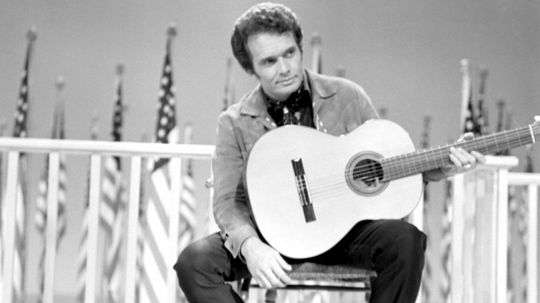 Merle Haggard sitting onstage with guitar
