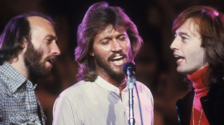 The Bee Gees singing into microphone on stage.