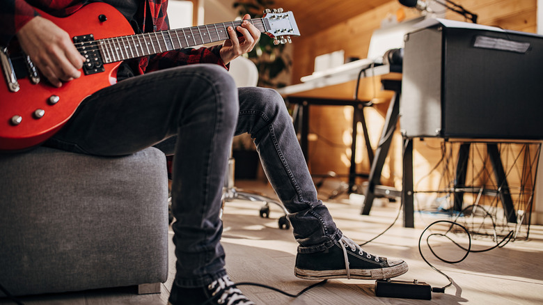 Person playing guitar at home with pedal and amp
