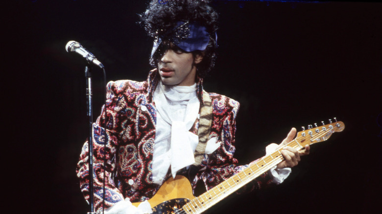 Prince on stage playing guitar in a garish outfit.