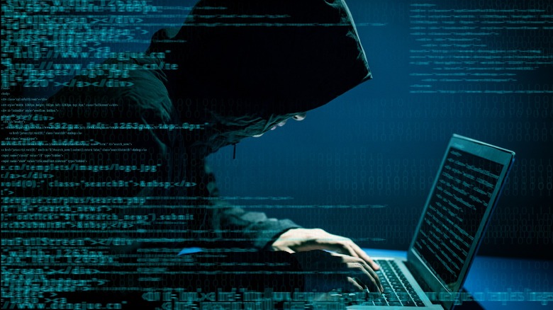 Hooded person typing on laptop with code overlapping