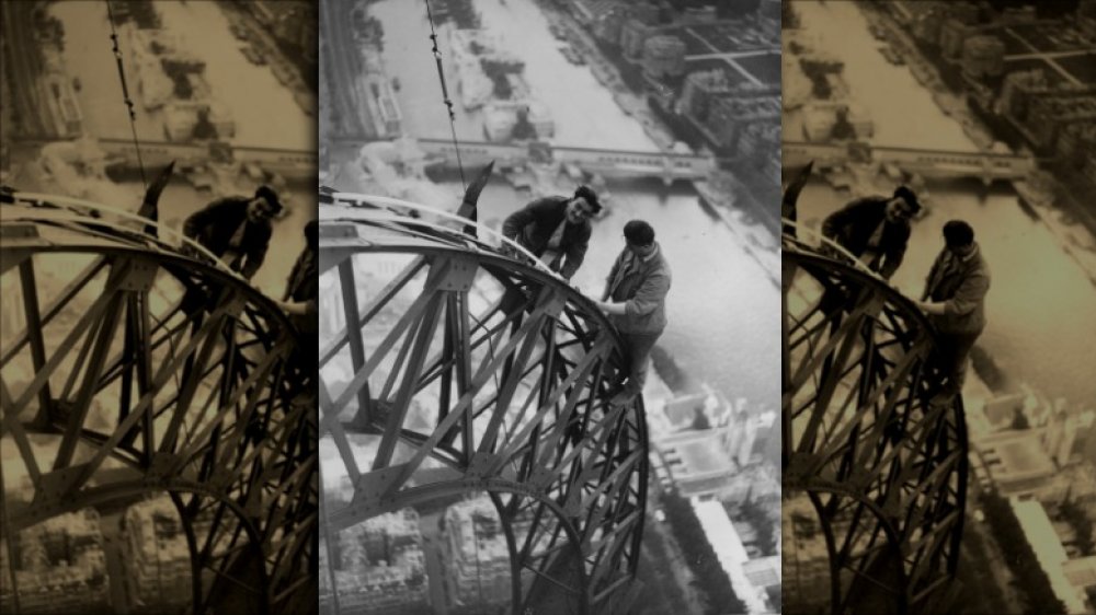 High above the River Seine two electricians work on the lights on the Eiffel Tower which will illuminate the Paris Exhibition at night.