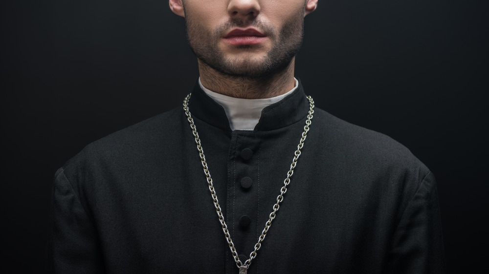 Ominous priest standing against dark background