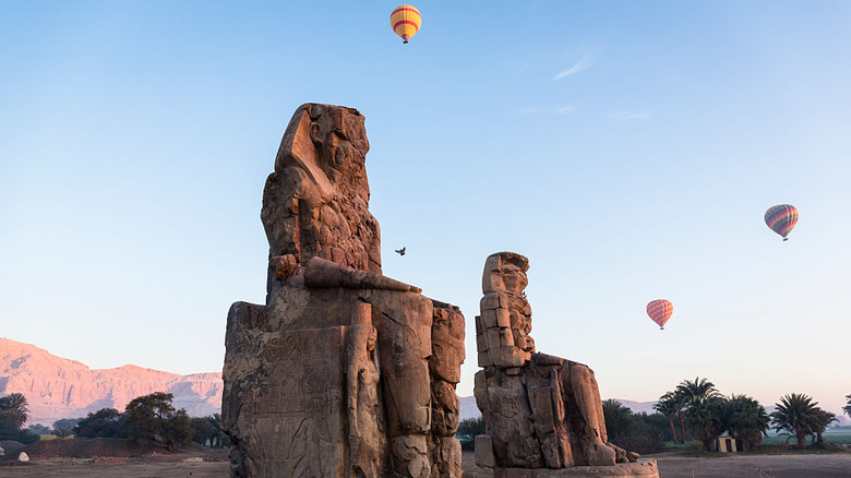 hot air balloons flying over statues in egypt