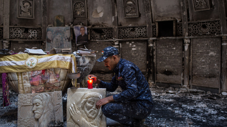 Syrian Christian soldier lighting candle in burnt church
