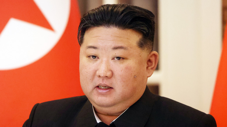 Kim Jong-Un in black suit speaking in front of flag