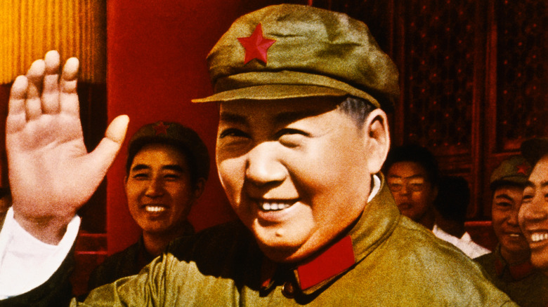Mao Zedong smiling and waving in crowd wearing communist hat