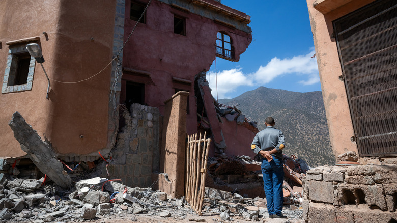 man looking at crumbled house