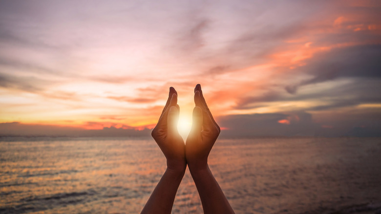 a woman frames a sunrise with her hands