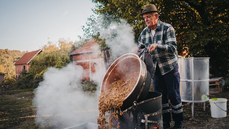 Man tipping pot of home distilling ingredients outdoors