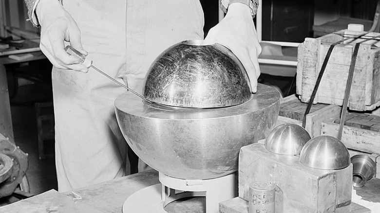 Man prying open metallic hemispheres with screwdriver in lab