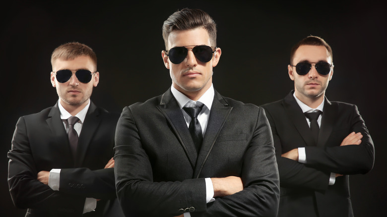 Three men in black suits with sunglasses on dark background