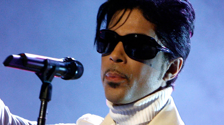 Prince wearing a white turtleneck and jacket with sunglasses while performing