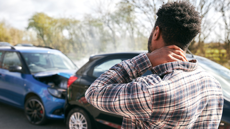 Person holding neck looking at two damaged cars after accident