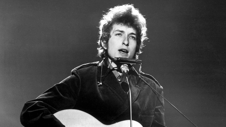 Bob Dylan singing into a microphone and playing acoustic guitar.