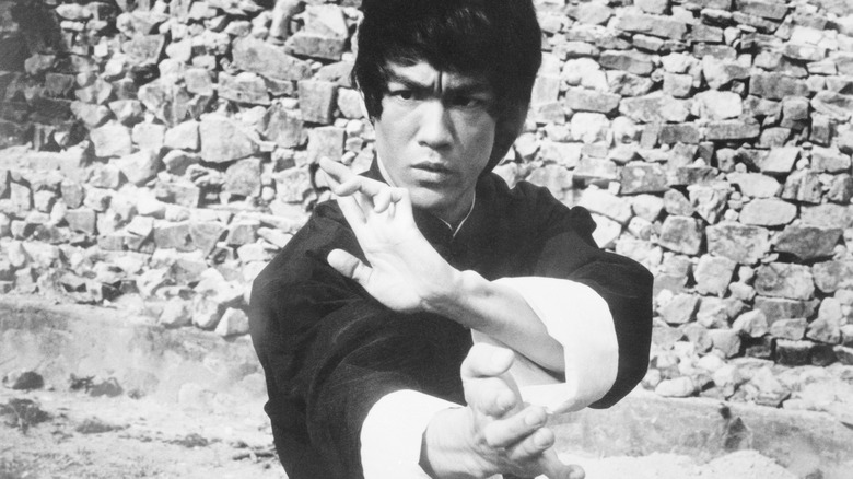 Bruce Lee hands raised fighting stance by stone wall
