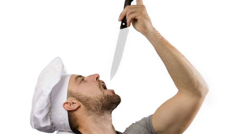 man holding knife above open mouth