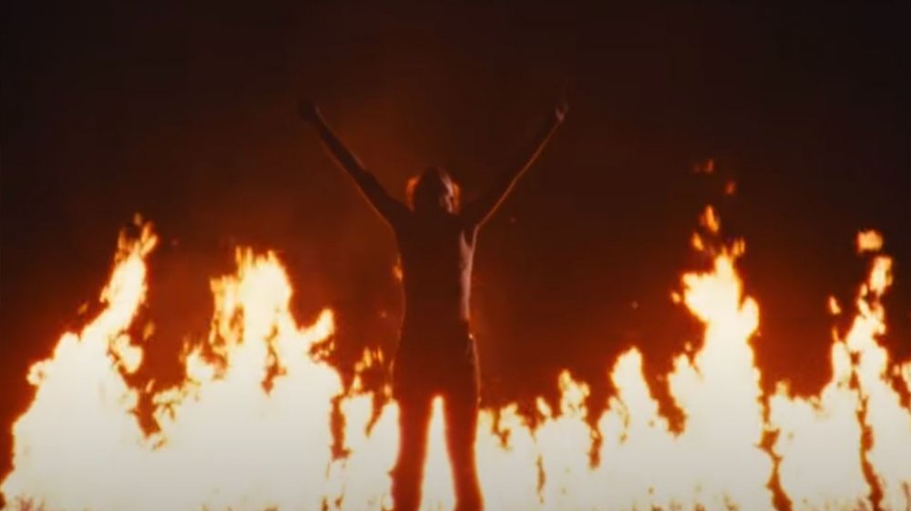 The young man Jeremy lifts his arms in front of fire in "Jeremy" by Pearl Jam