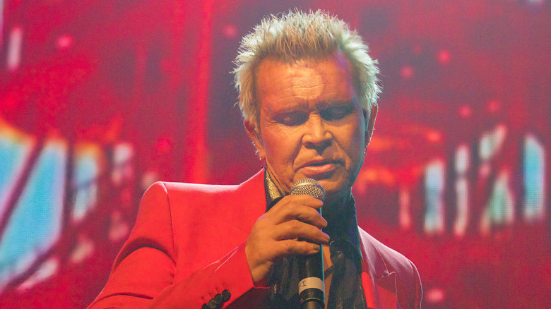billy idol looks down while singing against red backdrop