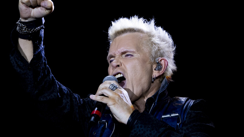 billy idol holding up fist and singing on stage