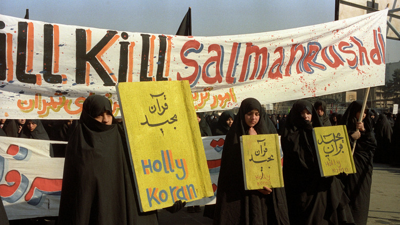 Protesters in Tehran holding protest signs by banner calling for death of Salman Rushdie