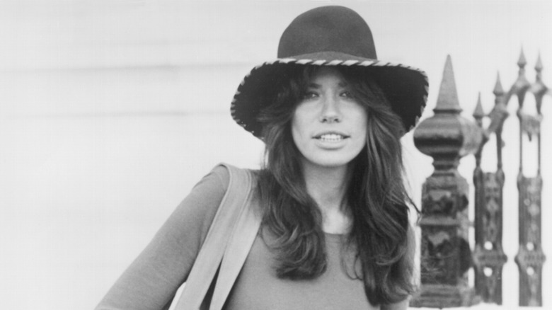Carly Simon smiling wearing a widebrim hat by railing