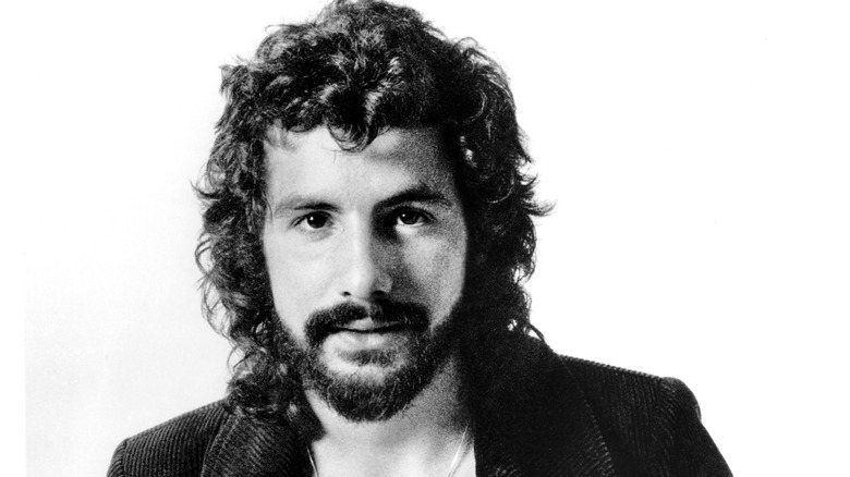 Cat Stevens smiling with beard, long hair, and jacket white background