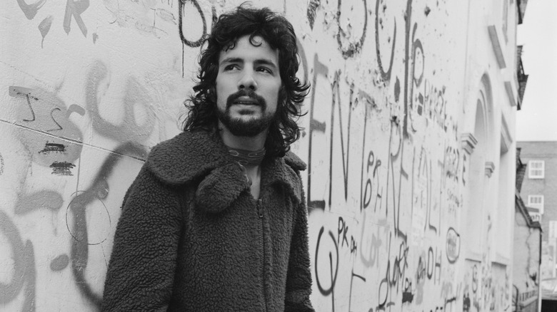 Cat Stevens standing in front of a grafitti-covered wall