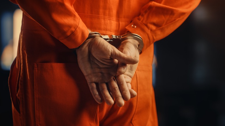 A man's wearing an orange jumsuit with his hands cuffed behind his back