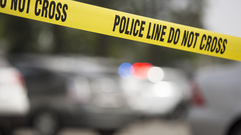 Crime scene tape with police vehicles in background